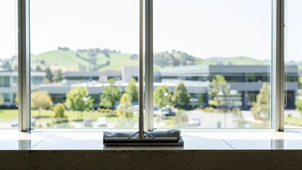 Floor-to-ceiling lobby glass with a squeegee on the ledge and green hills outside